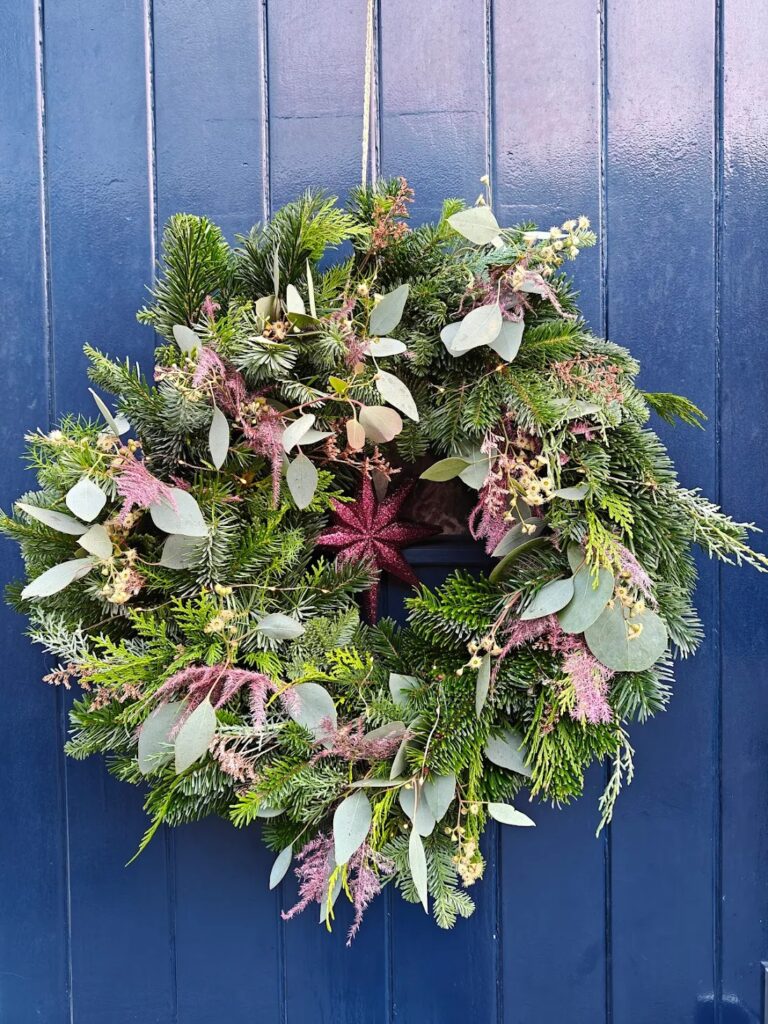 een kerstkrans met kerst groen op een blauwe deur gemaakt in een kerst workshop bij Bloom & Beyond